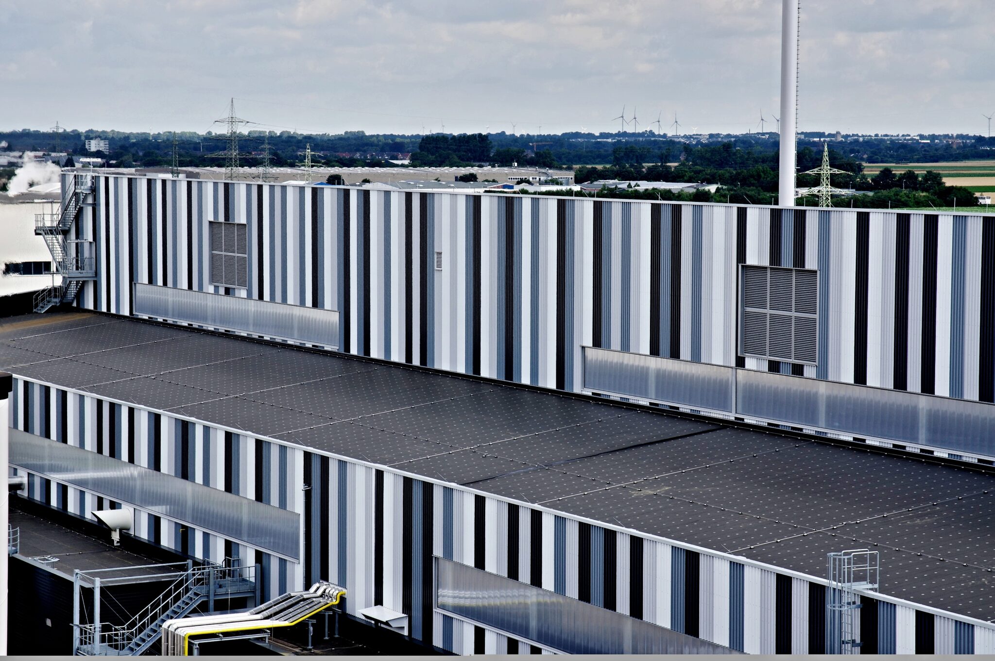 Luftaufnahme des grossen Industriedachs mit Windkraftanlagen im Hintergrund, Referenzprojekt Aluminiumwerk Grevenbroich von HDG Dachtechnik